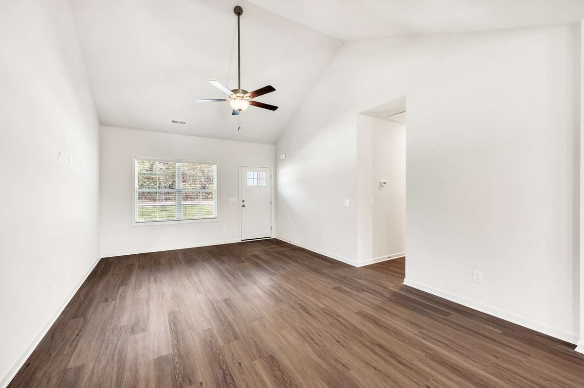 Bright and airy living area with vaulted ceilings and rich wood-look floors. The open layout and large window fill the space with natural light, creating a warm and inviting atmosphere perfect for relaxing or entertaining.