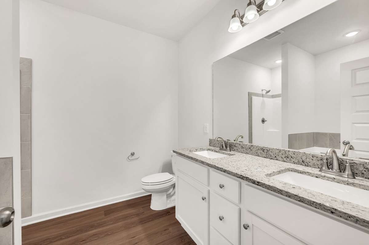 The classically white bathroom appeals with clean, clear lines and a crisp ambience, featuring a double vanity with granite countertops, undermount sinks, and brushed-nickel finishes.