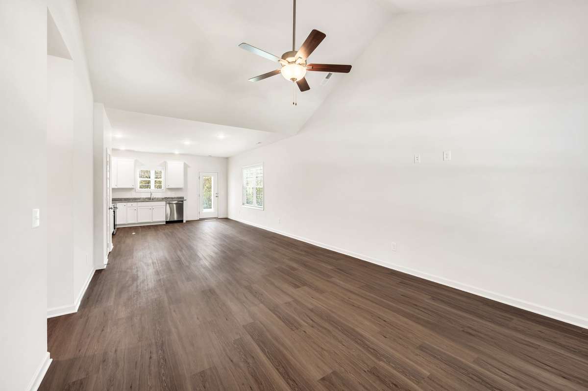 Bright, open-concept living space with vaulted ceilings and wood-look flooring. The airy layout flows seamlessly into the kitchen, creating the perfect setting for entertaining or relaxing. Modern finishes and natural light enhance the spacious feel.