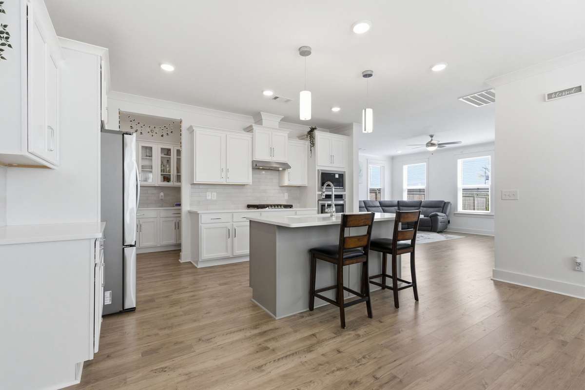 True chef's kitchen featuring a contrasting gray island, white shaker cabinets, and built-in stainless steel appliances.