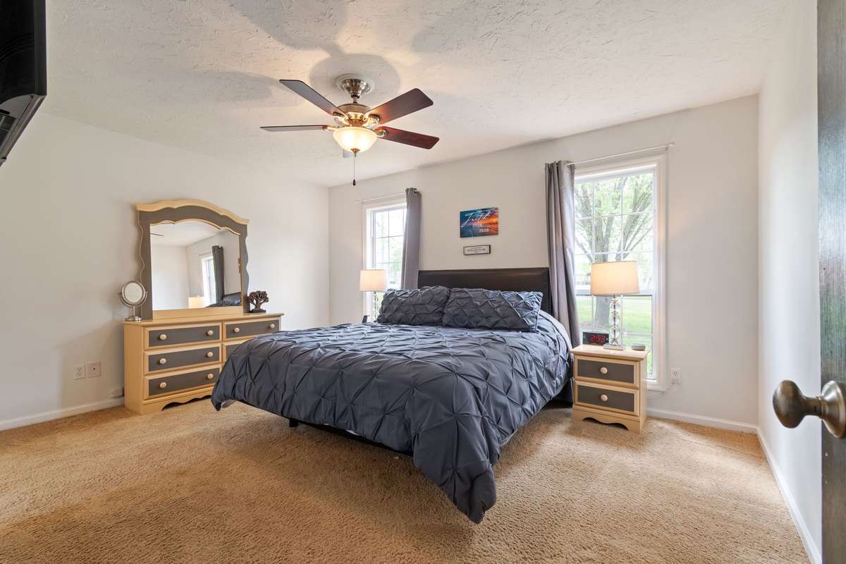 The spacious and comfortable primary bedroom features soft carpet, a ceiling fan, and great natural light from two windows.