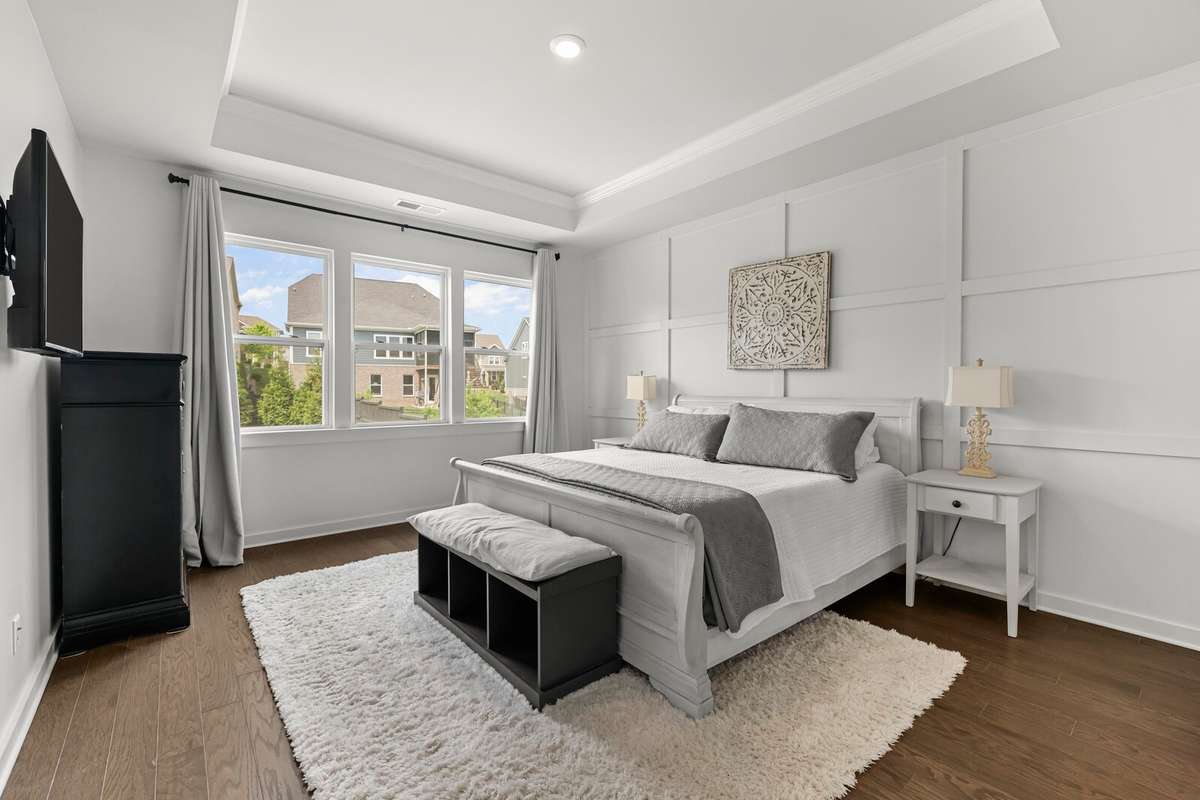 Located on the first floor, the primary suite is graced by hardwood floors, trey ceiling, a wall of windows and a wood accent wall