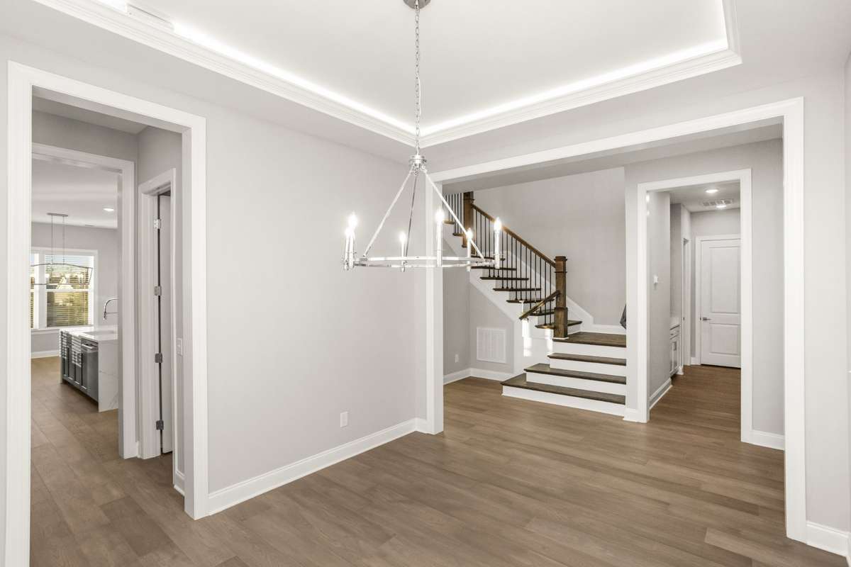 A view of the hall and stairs from the dining room, peeking into the hall that leads to the garage and laundry on the right and peek into the butler's pantry and kitchen on the left