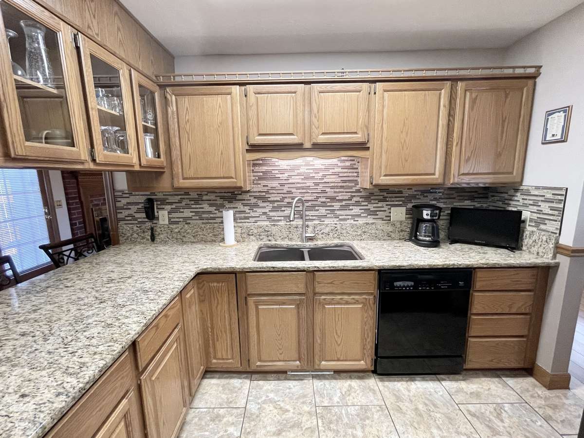The kitchen shines with expansive granite countertops, a sleek linear glass mosaic tile backsplash, and large-format tile flooring for a modern, sophisticated look.