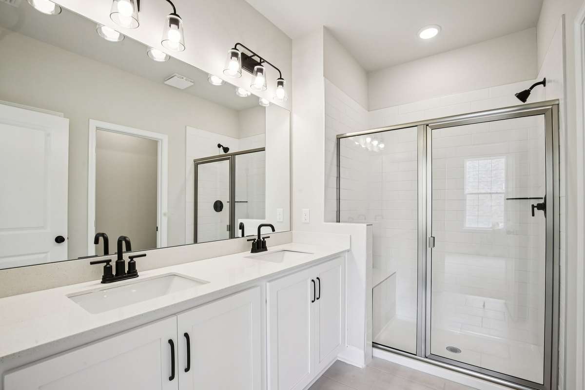 The primary bath features tile flooring, dual sinks with quartz countertops, and a tiled shower with a convenient bench seat, combining style and functionality.