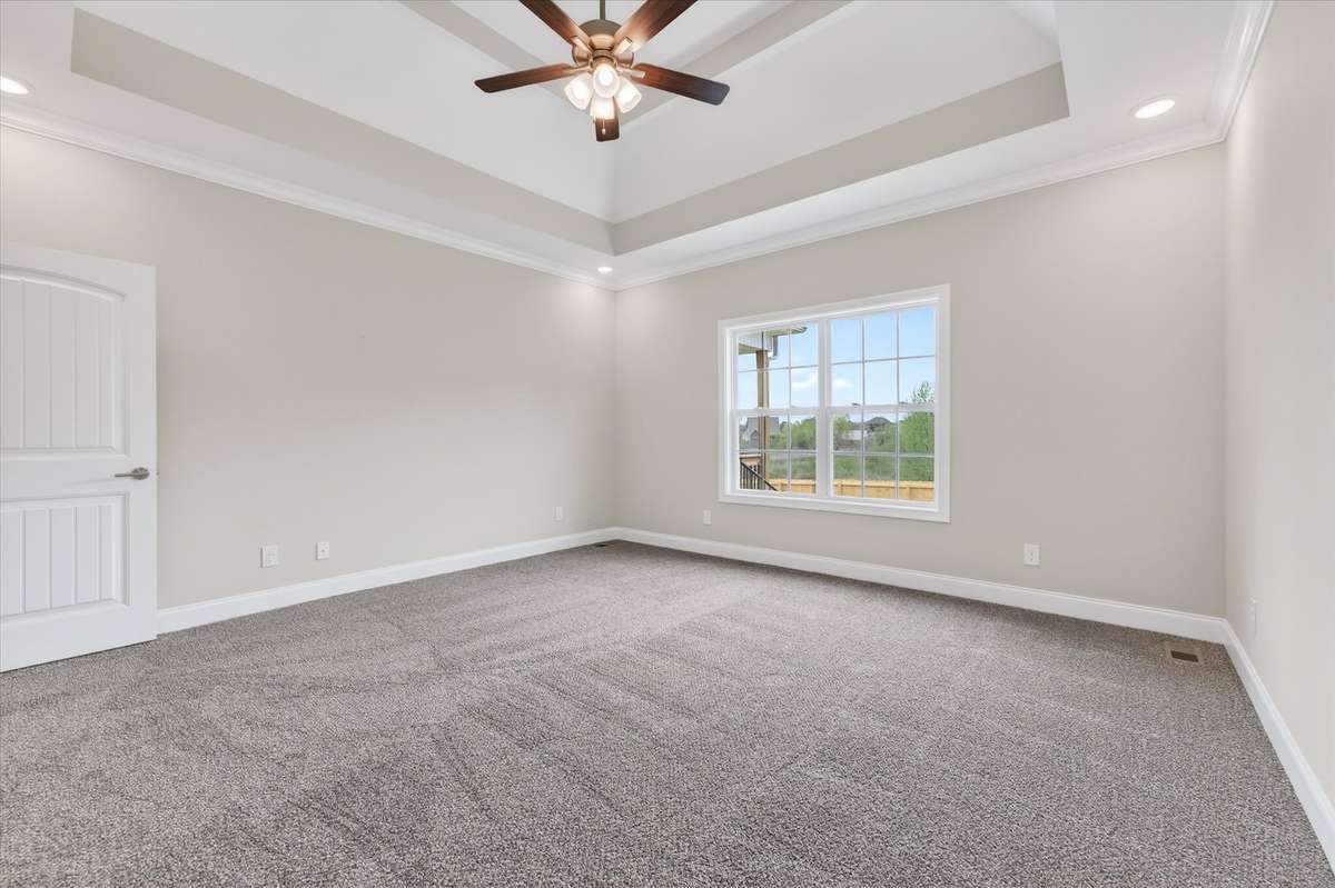 Spacious primary bedroom with tray ceiling and plush carpet