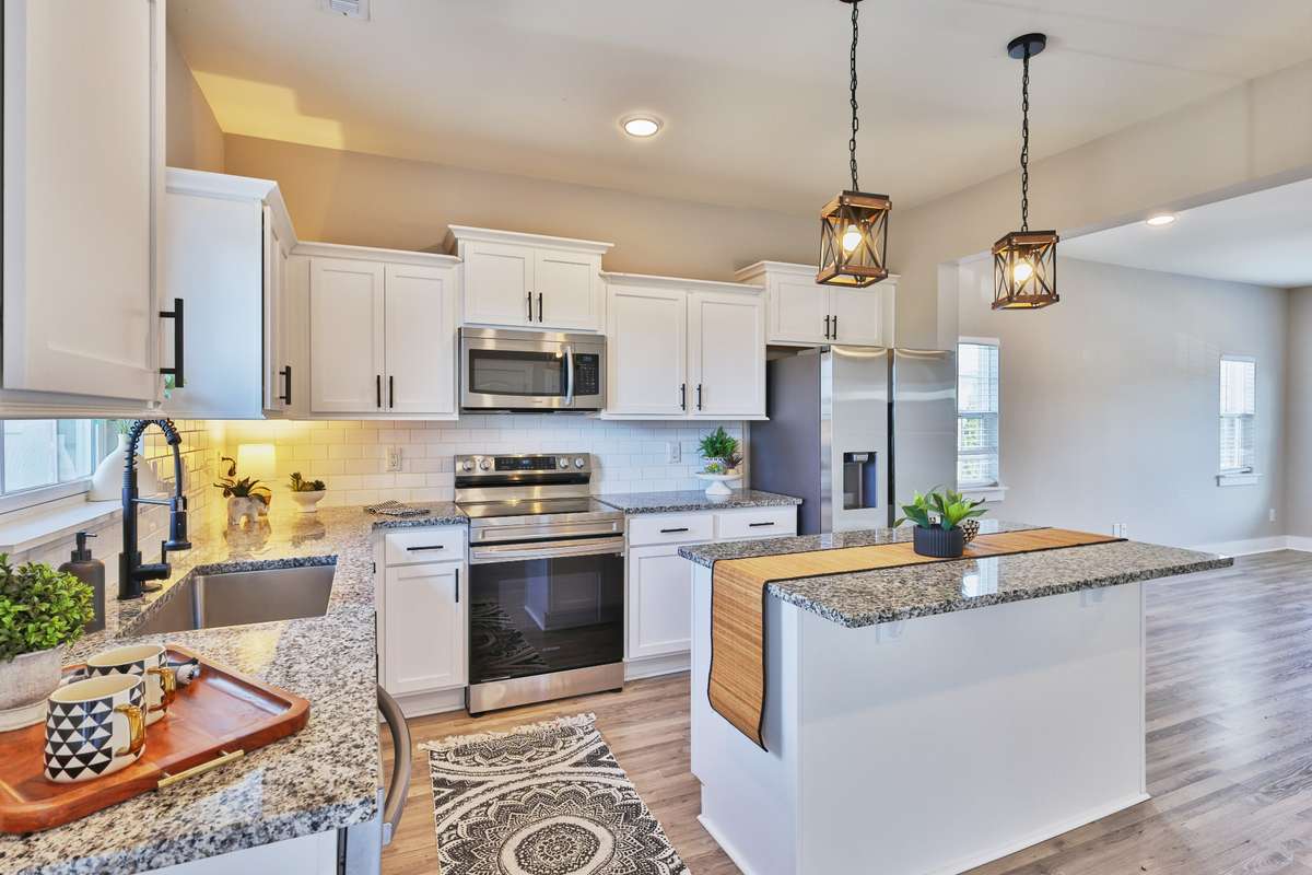 We love the staggered upper cabinet profile with crown molding, along with the tile backsplash, deep single bowl stainless sink with disposal, black arched pull down faucet with sprayer, and coordinated island pendants and cabinet pulls.