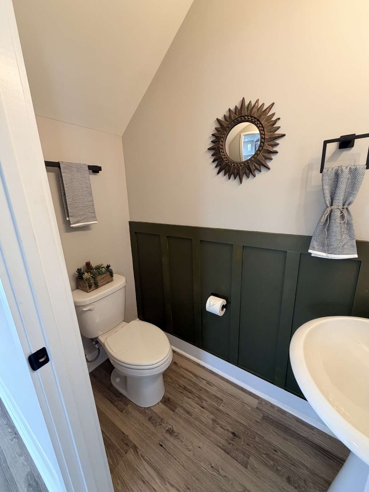 This home features custom upgrades including designer lighting, upgraded knobs and pulls, and custom shower doors. The deep olive green wainscoting in the main floor half bath adds a warm, stylish pop of color while keeping the space bright.