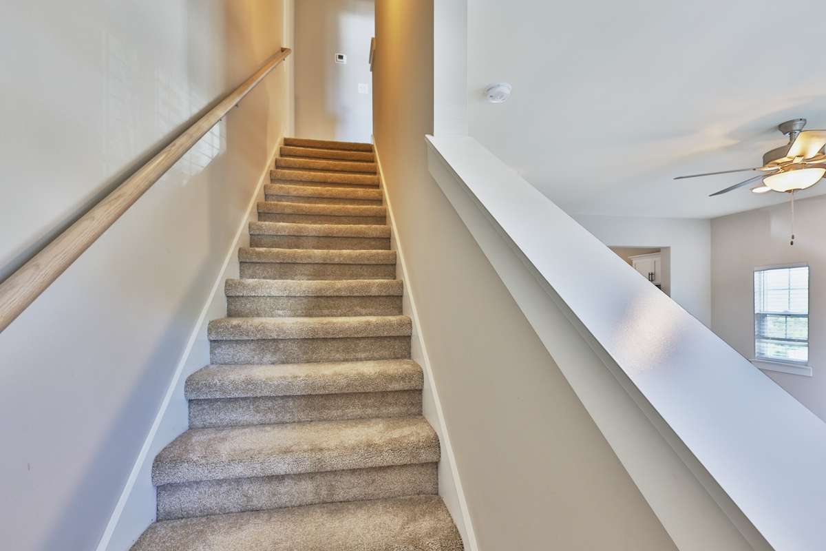 Carpeted stairwell with long wooden handrail leads to second floor landing and hallway.