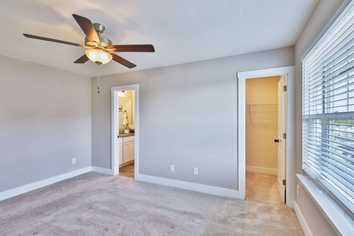 Primary bedroom has ceiling fan, full bath, and two lighted walk-in closets. The larger closet is shown, next to bath.