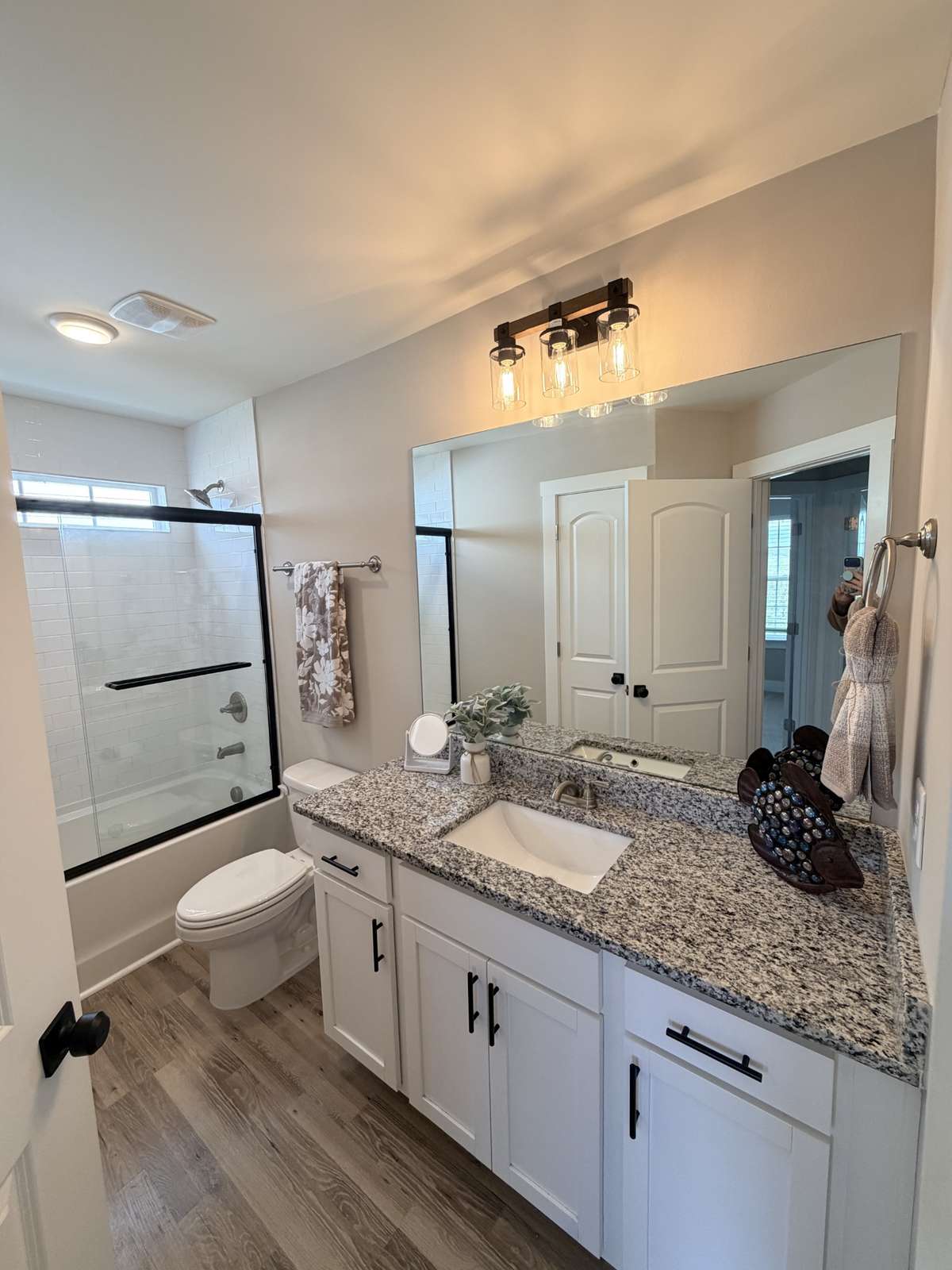 Hall bath, shared by bedrooms two and three. Features updated lighting, combo tub/shower, shower door, hardware. Granite counter with wide undercount sink, linen closet behind entry door.