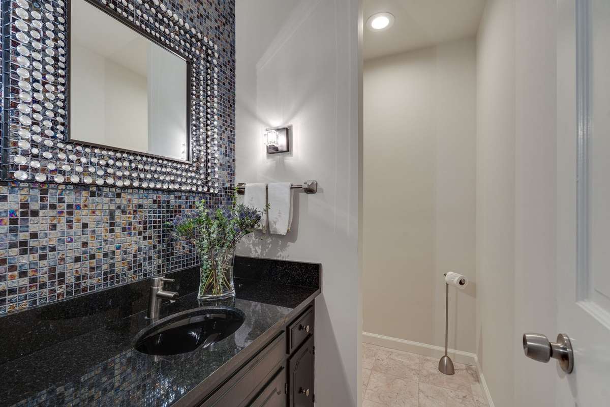 Powder room on the main floor with a custom vanity, a full wall tiled backsplash and custom lighting