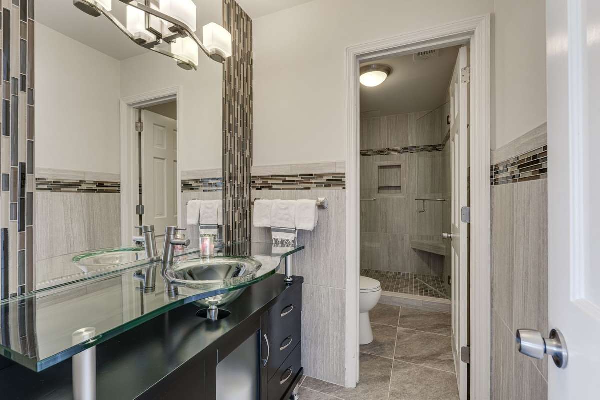 The hallway bath has a door separating the vanity area from the shower and features custom tiling on the floor and the walls