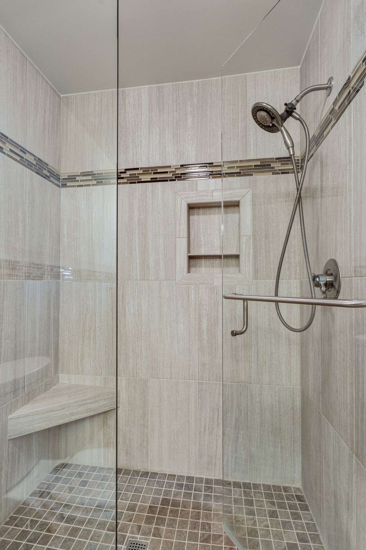 Walk-in large shower with a tiled floor, floor to ceiling tile surround and a frameless glass door