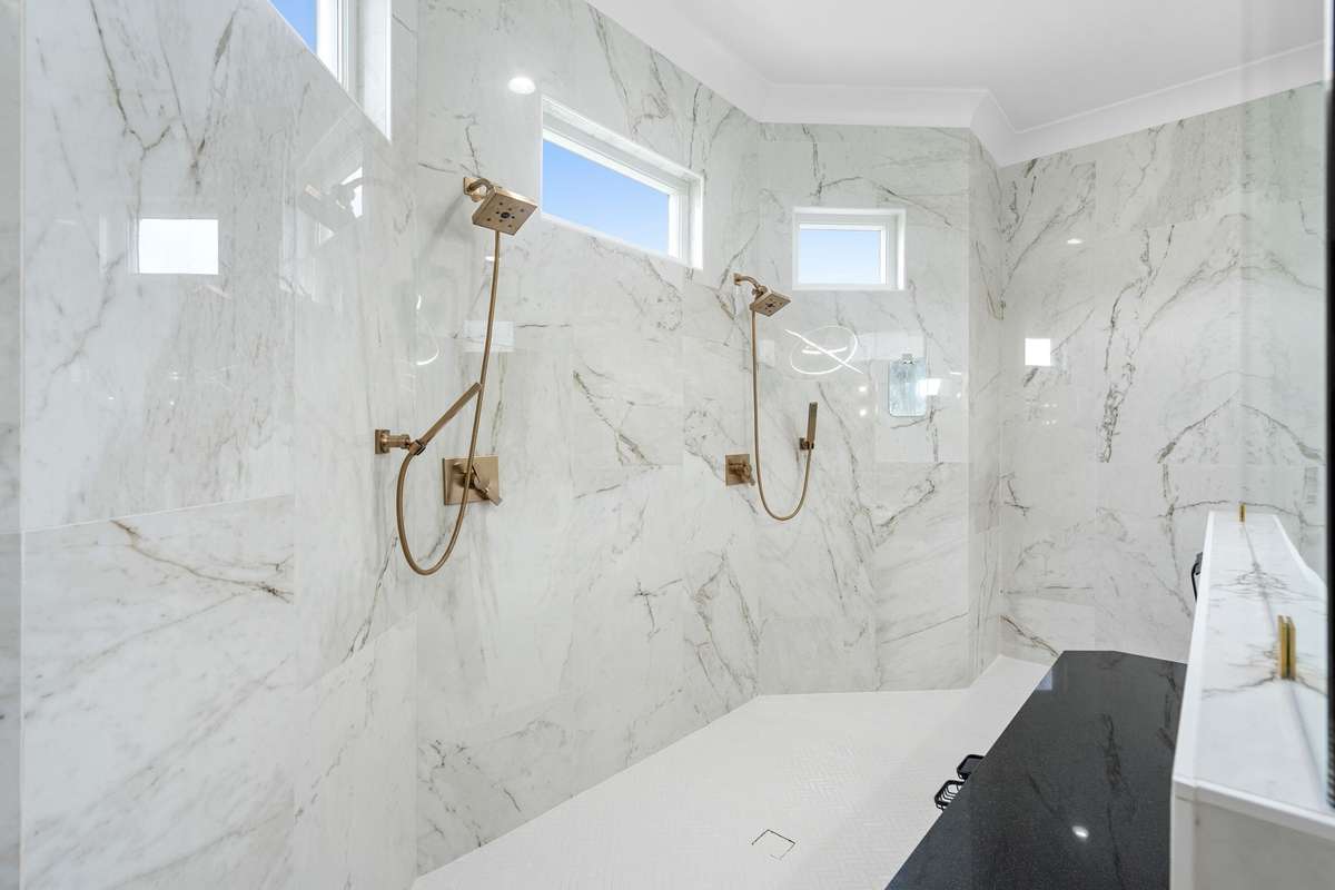 Expansive, glass-enclosed shower with dual rain heads and elegant marble surround for a true resort-style experience.