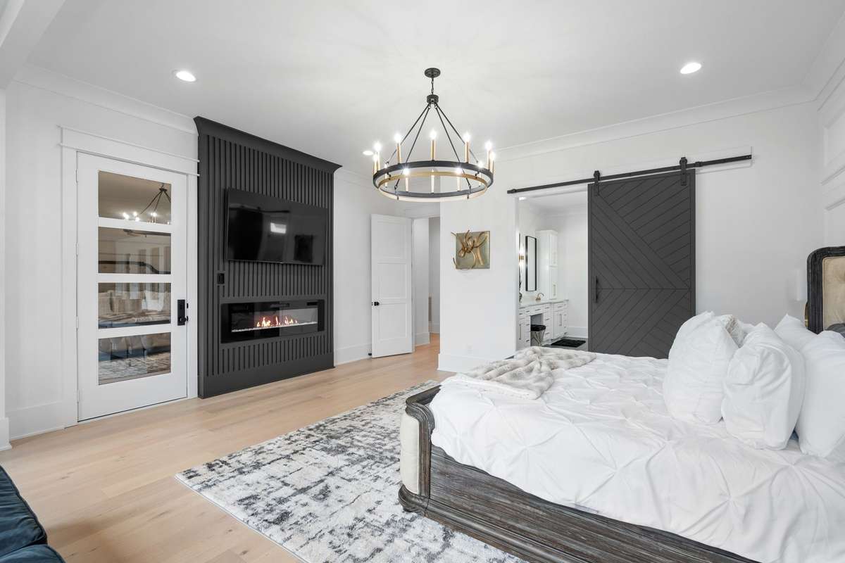 Primary bedroom with custom feature wall with electric fireplace, and sliding barn door entry into the primary bath suite. The door to the left leads to the spacious screened patio.