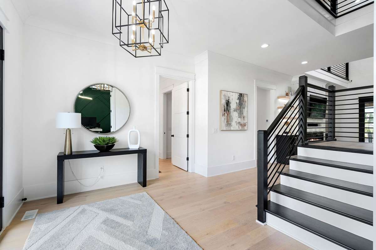 Light-filled entry with soaring ceilings, modern chandelier, and striking open staircase with custom railing.