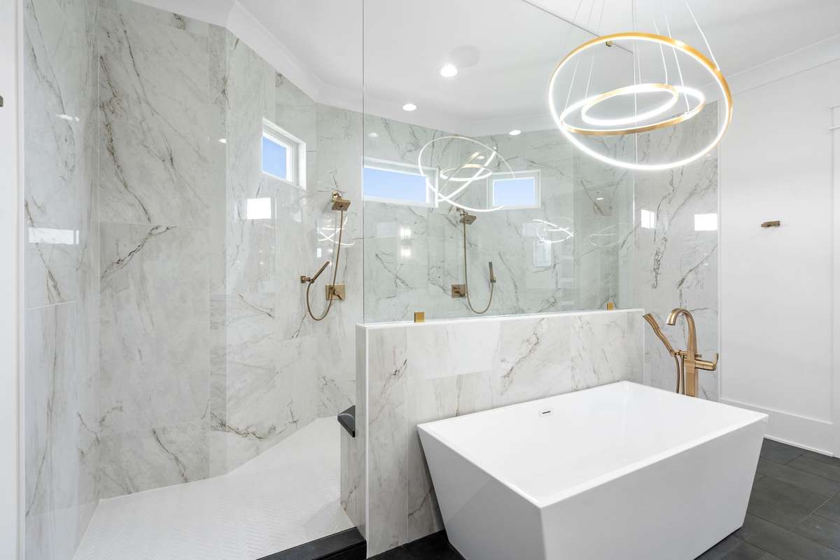 Luxurious freestanding soaking tub paired with a stunning dual walk-in shower featuring floor-to-ceiling marble and designer gold fixtures.