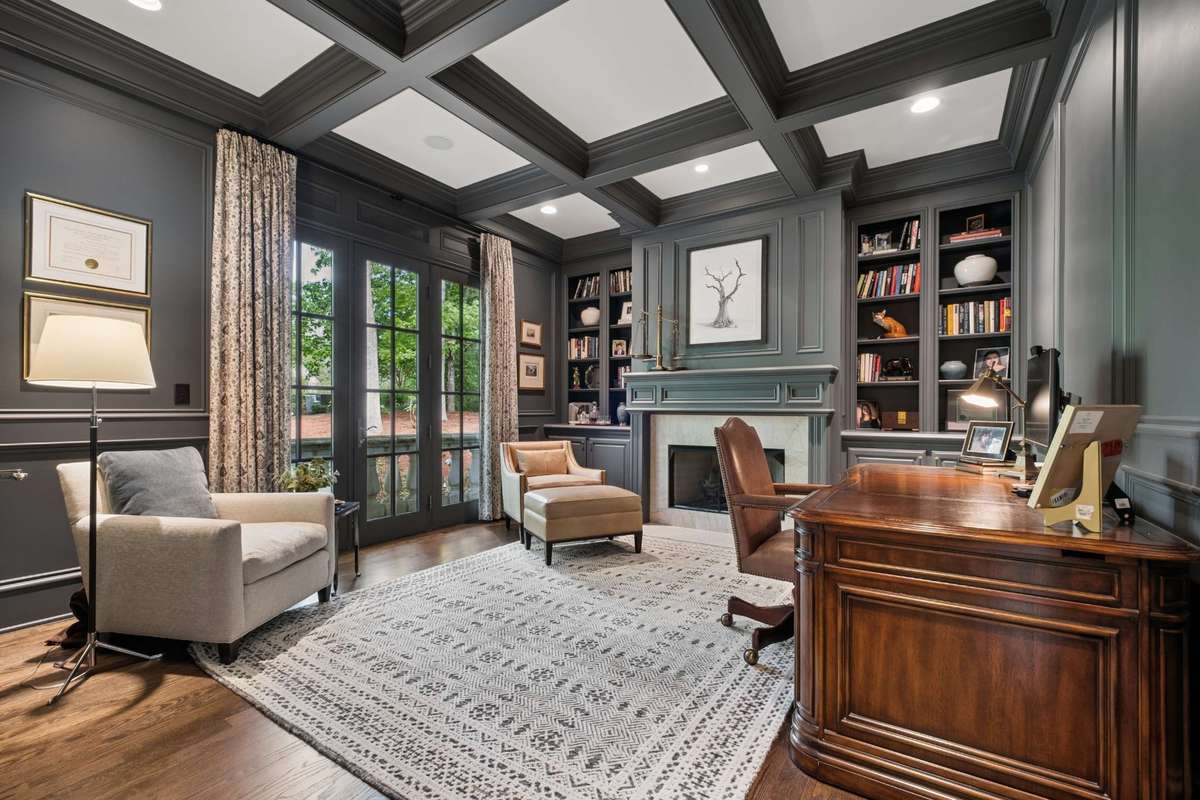 The handsome office/study features a coffered ceiling, a fireplace with gas logs, and custom built-in bookshelves with lower cabinetry—offering a spacious and refined setting ideal for working from home.