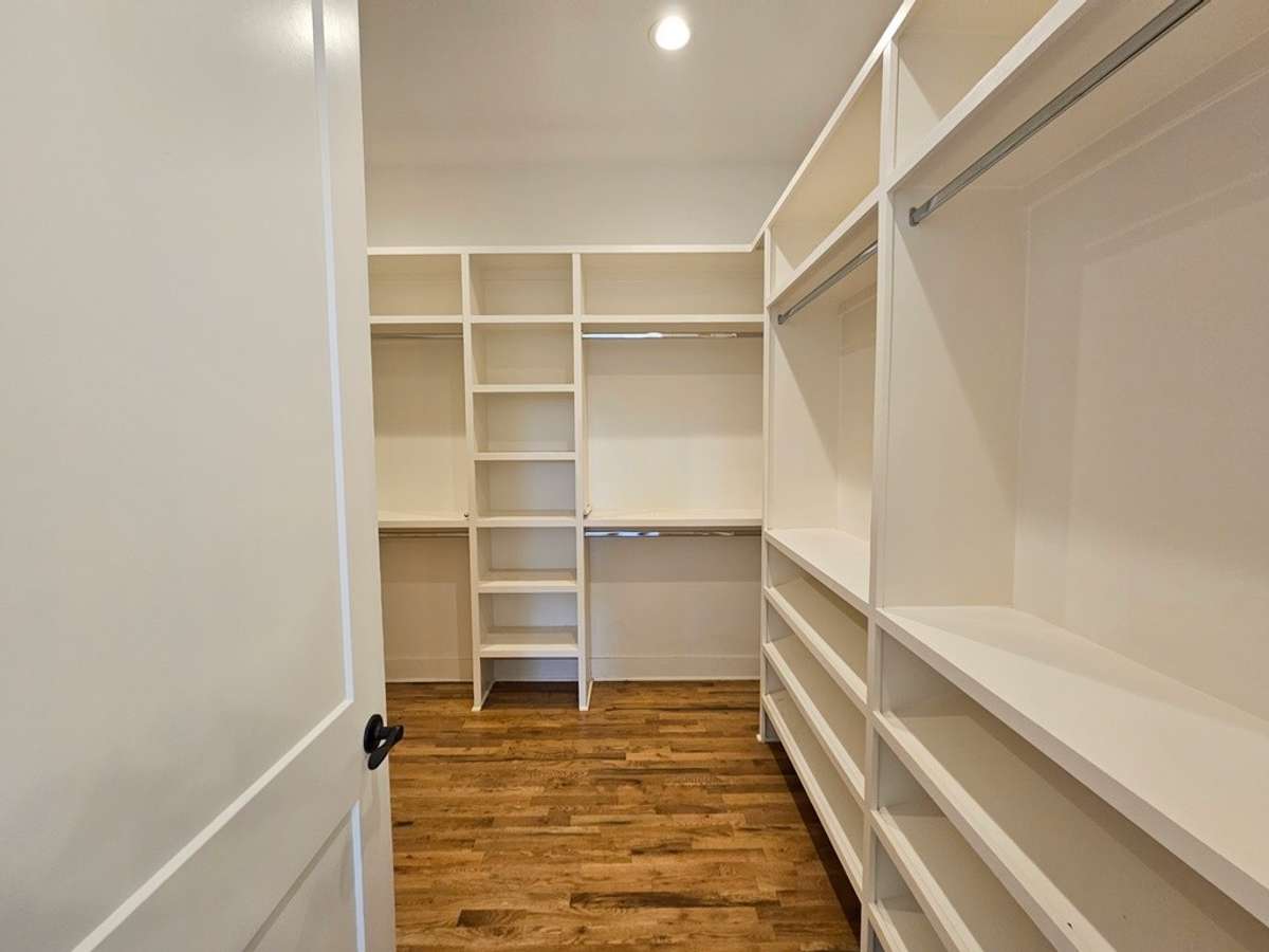 Large walk-in closet with lots of nooks for clothing, tilted shelves for shoes and hanging rods for clothing.