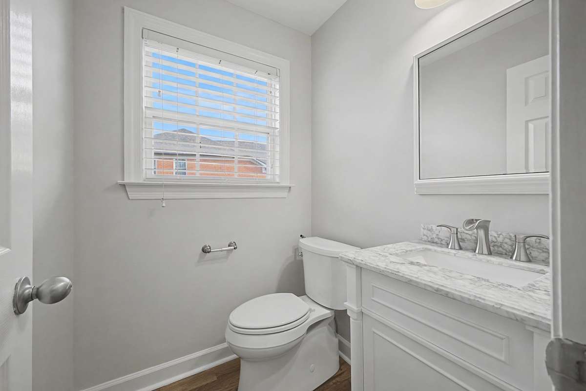 Main-level powder room conveniently located just off the living area and office, featuring granite countertops, hardwood flooring, and a well appointed design that adds both style and function to the space.