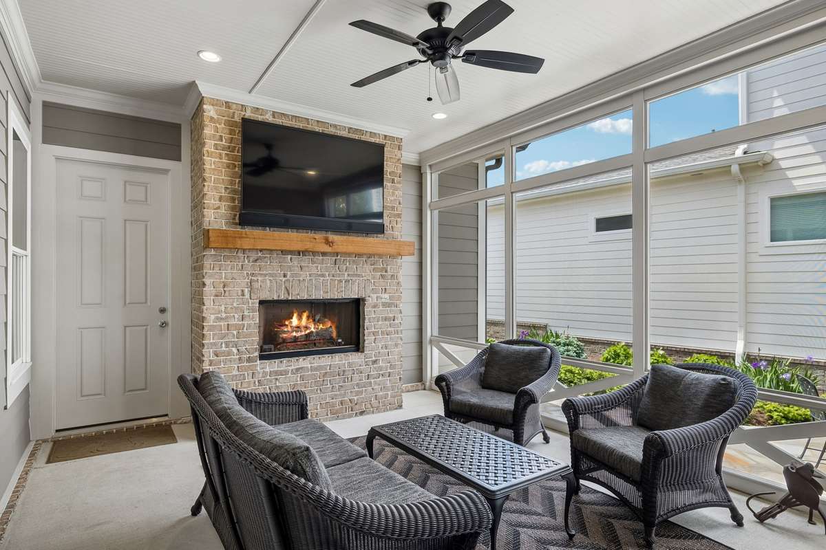 Inviting screened-in porch with a gas fireplace flows seamlessly to a knockout courtyard with flagstone walkways, patio space, and classic black metal fencing.