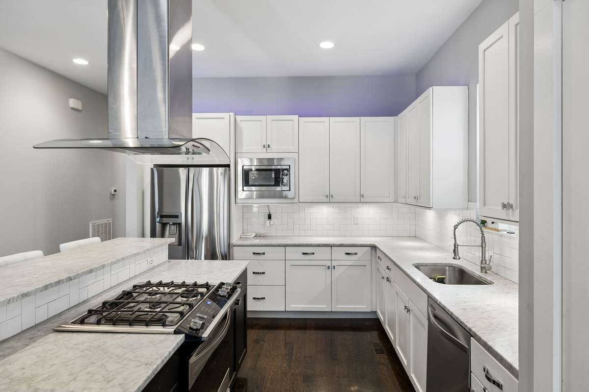 Bright, modern kitchen featuring so much counter space, a large sink beneath a window, abundant cabinetry, a pantry, stainless steel appliances, and a gas range with vent hood.