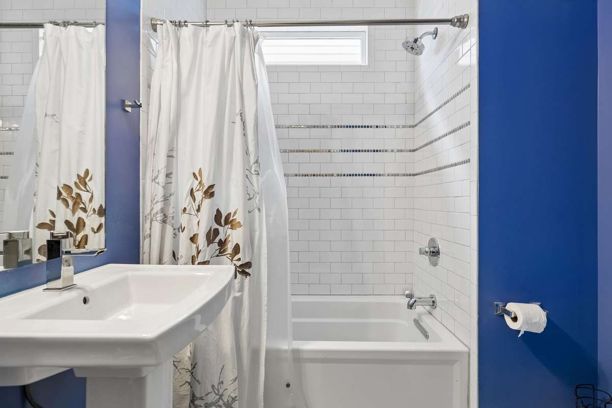 First-floor full bath featuring a tiled tub/shower combo, modern fixtures, and a pedestal sink.