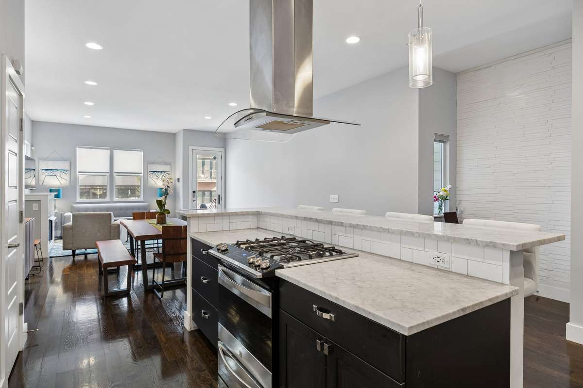 A bar island with gas range, pendant lighting above the bar seating, and a stainless steel hood vent overlooking the open-concept living and dining areas, creating a seamless flow for everyday living and entertaining