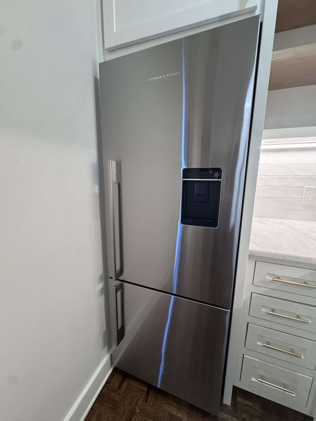 Custom-ordered Fisher & Paykel stainless steel refrigerator featuring a sleek water dispenser and convenient French drawer design.