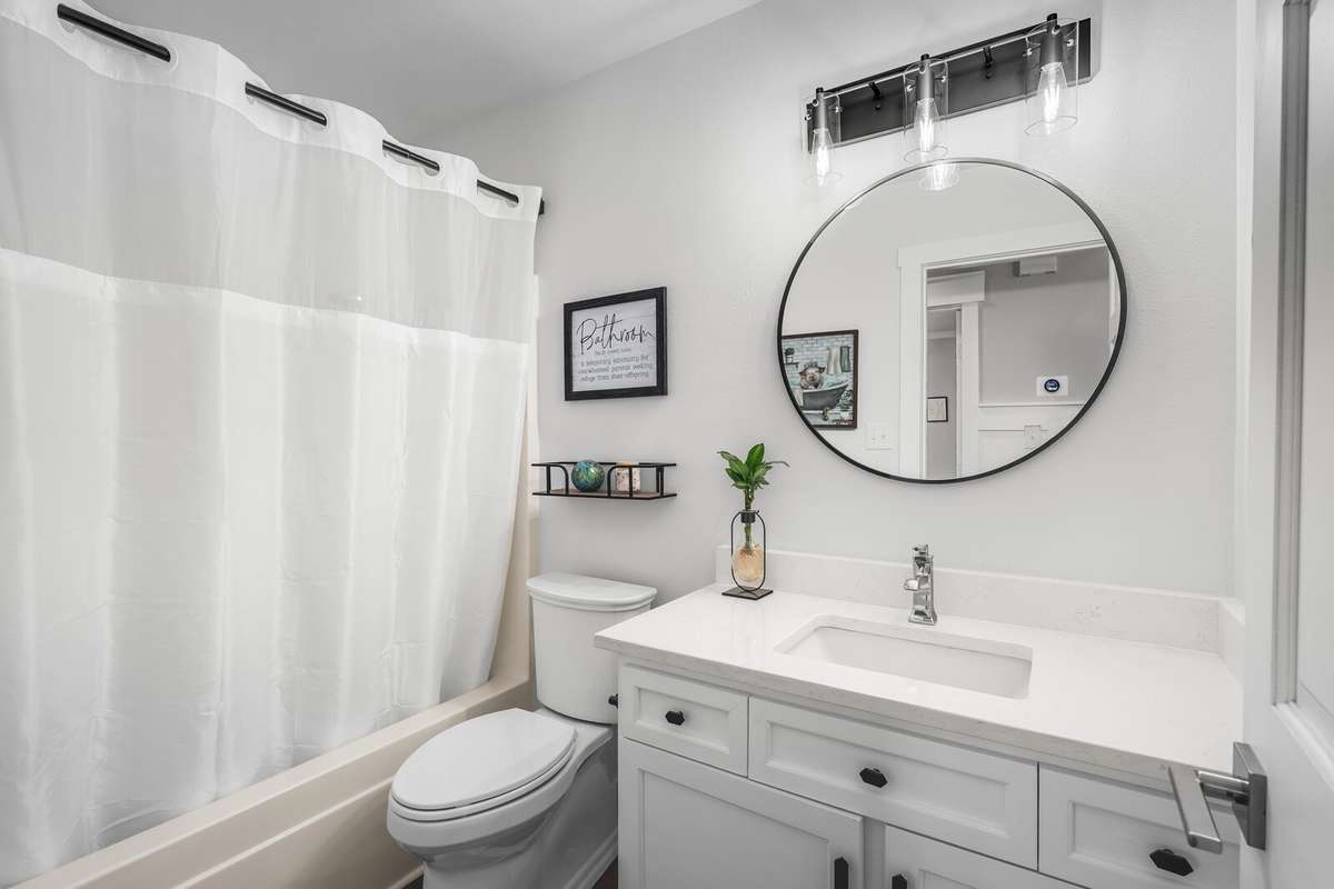 Additional full bath located in the hallway features a quartz vanity top, shaker cabinetry, round mirror, modern lighting and tub/ shower combo.