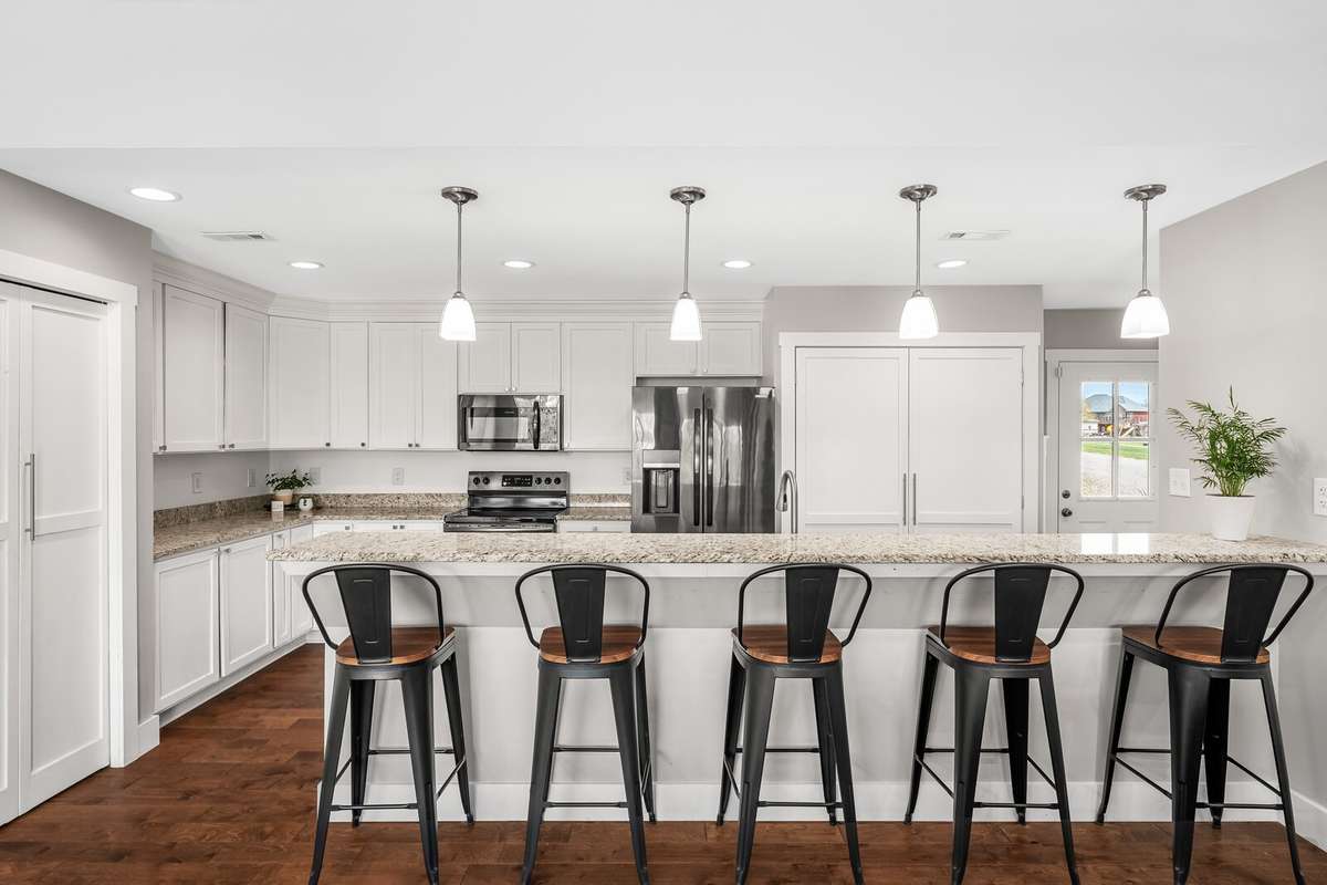 This kitchen is amazing! It features an expansive island seating, granite countertops, white cabinetry, and modern pendant lighting.