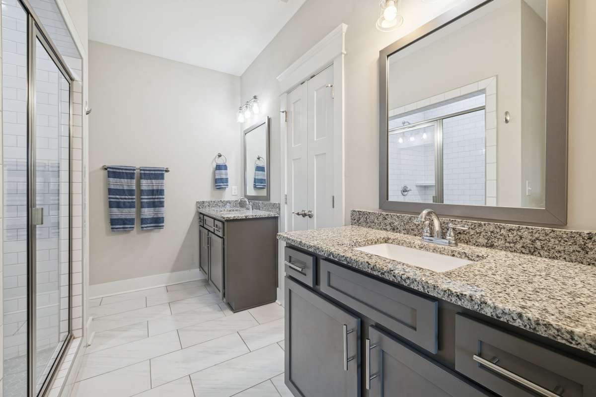 Separate vanities in the primary bathroom suite offer ample cabinet space and are topped with granite countertops, while the oversized flooring tiles provide a lovely accent to the tiled shower.