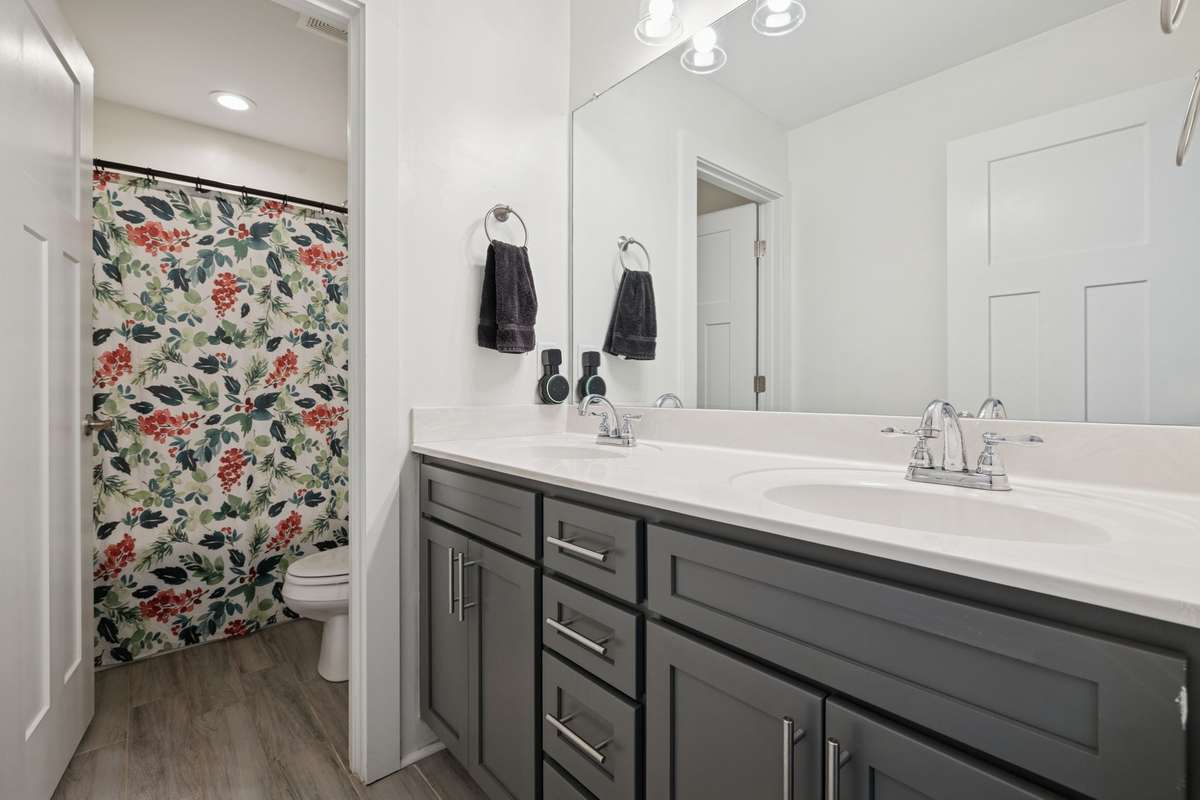 Positioned between the two secondary bedrooms, this bathroom offers convenience for multiple users, with a dividing door separating the double vanity from the shower and commode area.