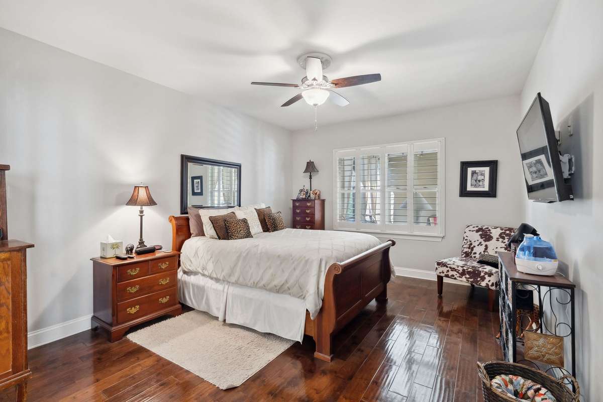 The primary suite features a large window with views into the enclosed breezeway, hard wood floors, plantation shutters, and a private suite bathroom.