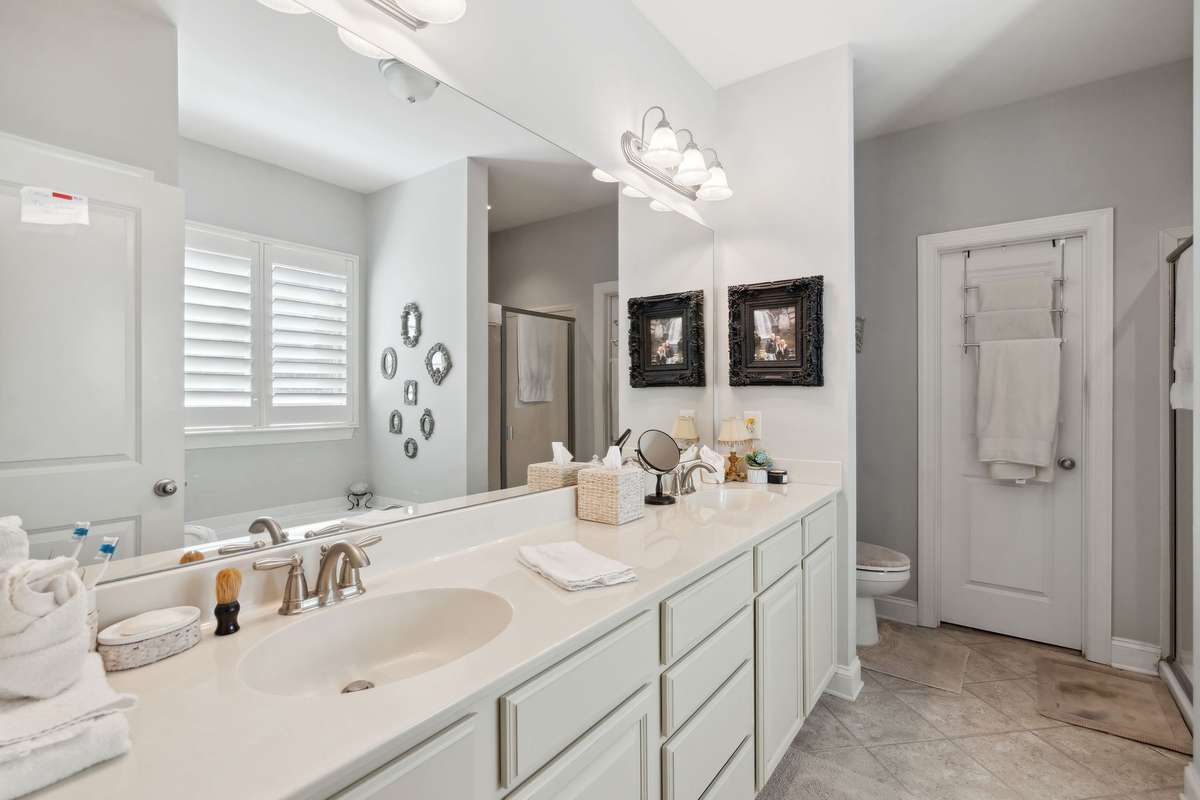 Primary Suite bathroom features double sink vanity, wall to wall mirror, tile flooring, large walk-in closet.