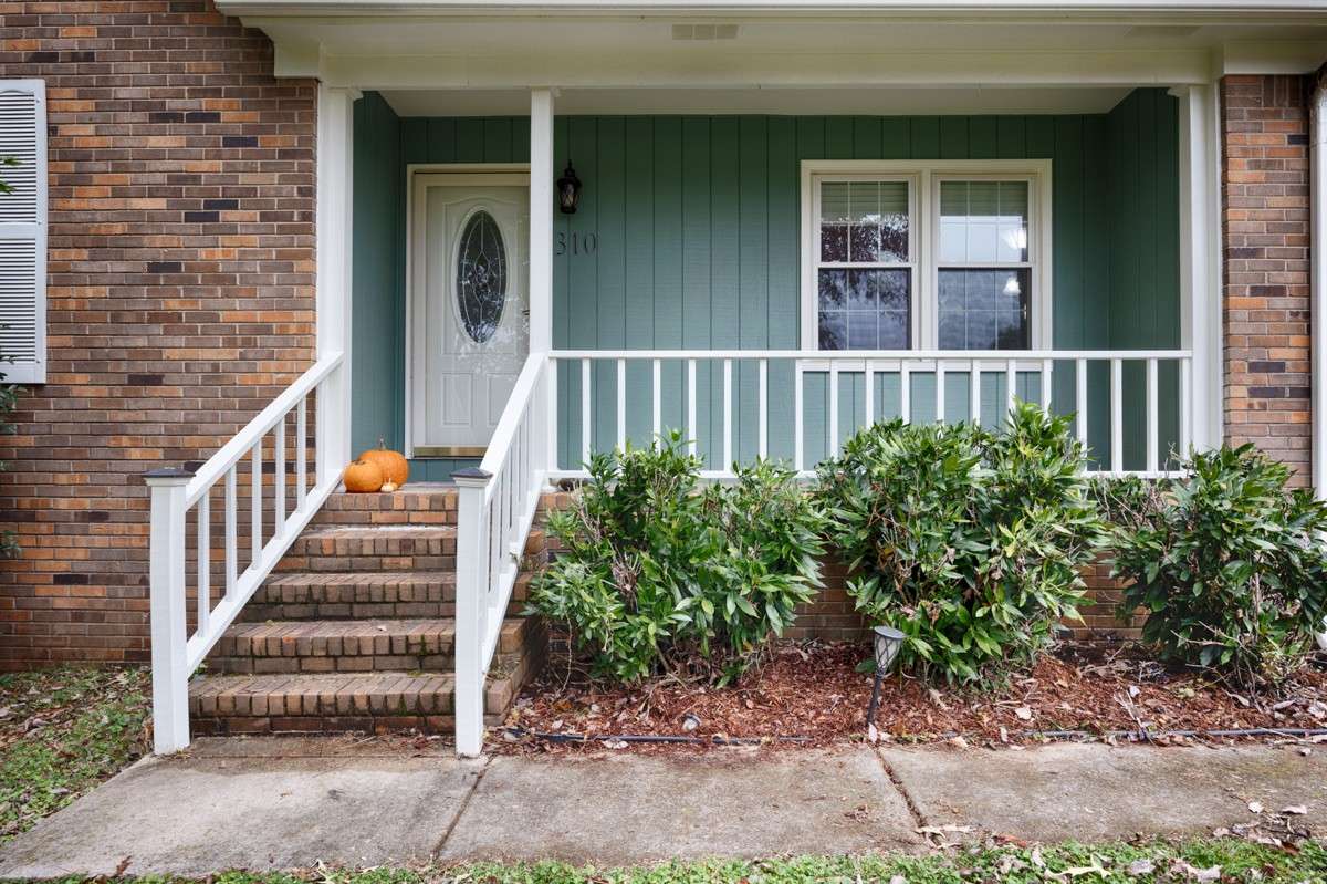 Covered front porch with concrete sidewalk, brick steps with railing
