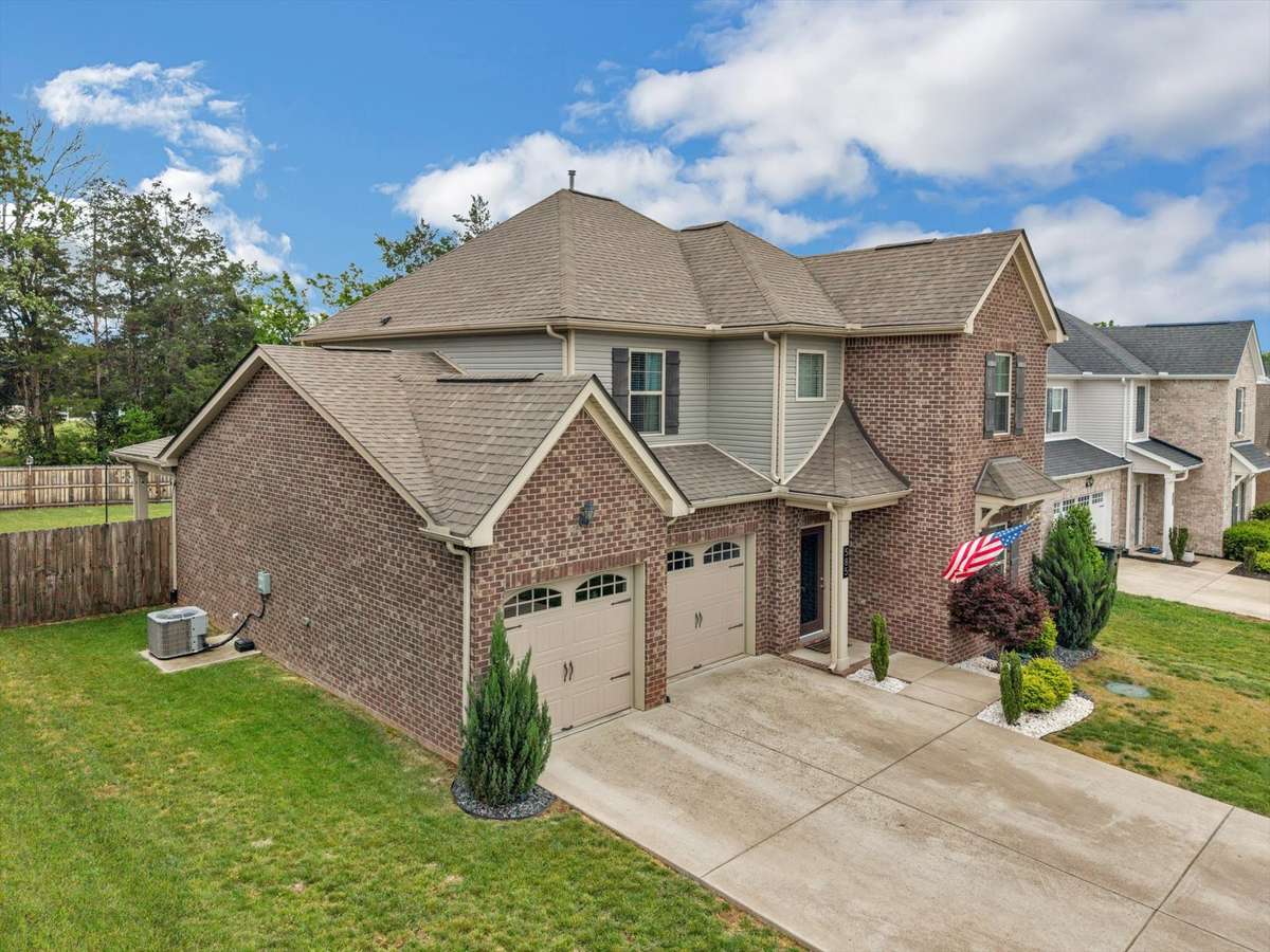 This side view shows a large driveway, a mostly brick home with some privacy at the back of the lot.