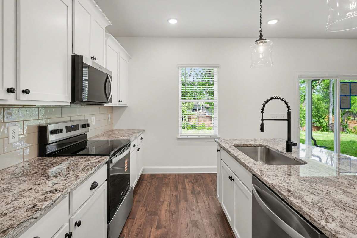 Bright, designer kitchen featuring white shaker cabinetry, granite countertops, stainless steel appliances, subway tile backsplash, and stylish pendant lighting.