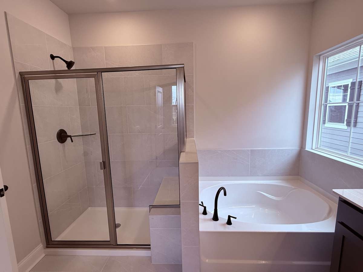 The primary bathroom is thoughtfully designed for both style and comfort. It includes a tiled shower with a built-in bench, perfect for relaxing or convenient daily use, alongside a deep soaking tub ideal for unwinding after a long day.