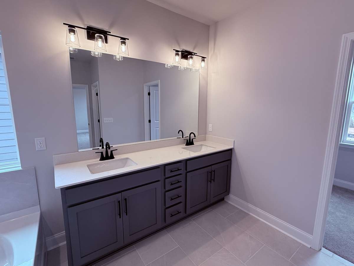 The primary bathroom is beautifully designed with tile flooring and dual sinks set in quartz countertops, combining functionality with a sleek, modern aesthetic for a spa-like retreat.