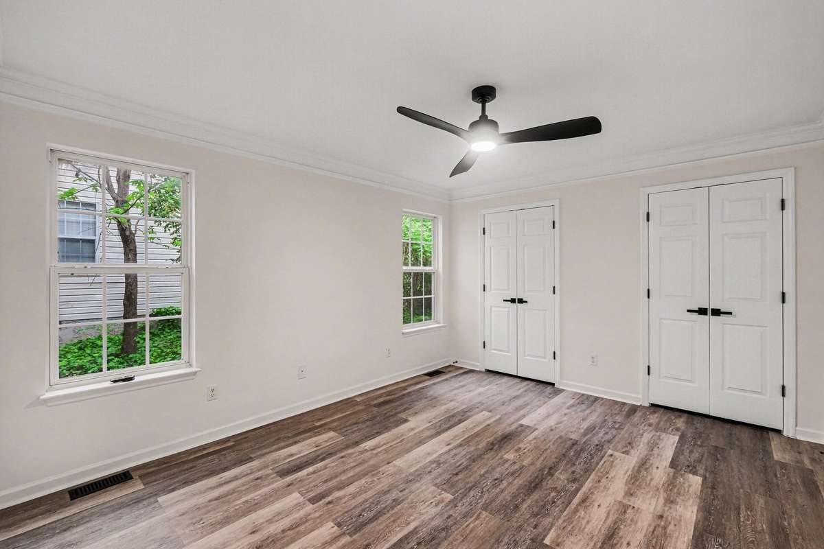 Relax in a main-level bedroom featuring brand-new, modern flooring and fresh interior paint. This retreat is accented by stylish crown molding, a new ceiling fan, and double closets with upgraded matte black hardware for a clean, designer look