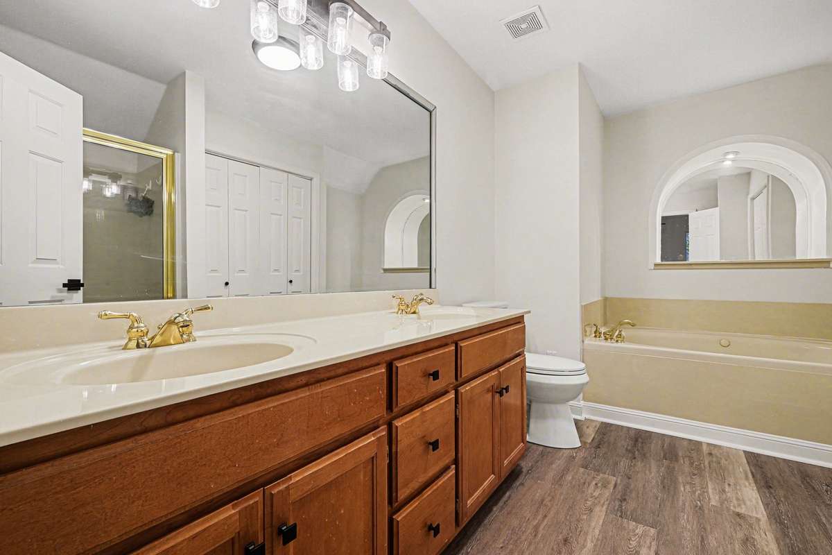 Well-appointed primary bath, boasting updated flooring and stylish new lighting. The dual-sink vanity provides convenience, while the oversized mirror and arched detail over the tub add a touch of character to this move-in-ready space.