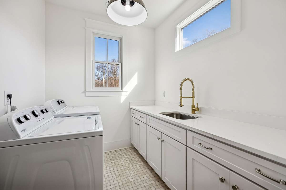 Large tiled laundry room with utility sink and ample cabinet storage