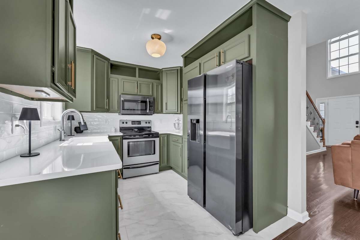 The kitchen features trendy green cabinets, gold accents, + tile flooring.