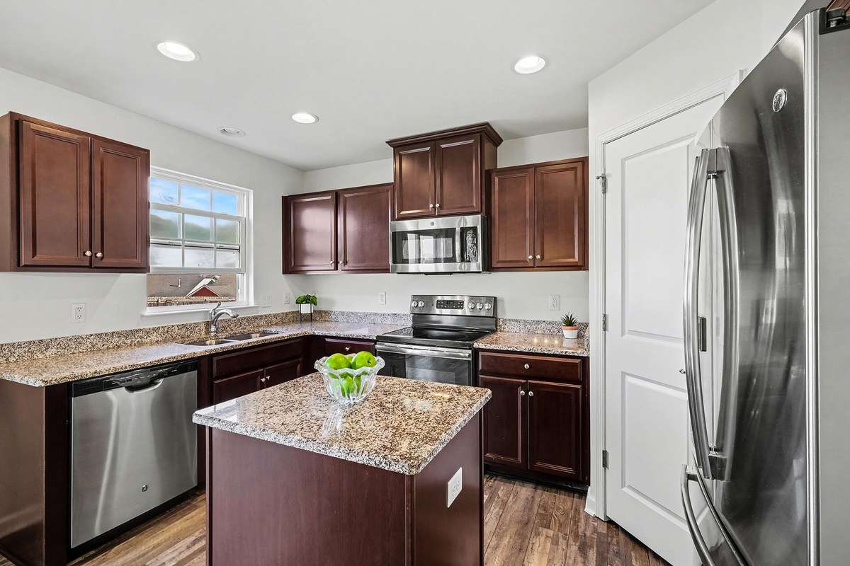 Granite counter tops, center island, pantry and stainless steel appliances in the kitchen. Window over sink looks out to new fenced back yard.