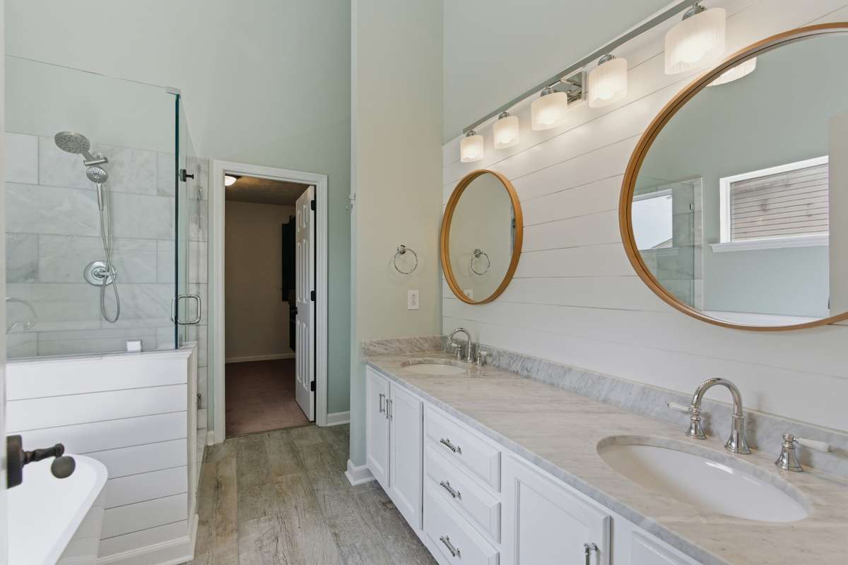 Spa-inspired owner’s bathroom featuring a freestanding soaking tub, glass-enclosed tiled shower, dual vanities with marble countertops, and abundant natural light—designed for everyday ease and quiet luxury.