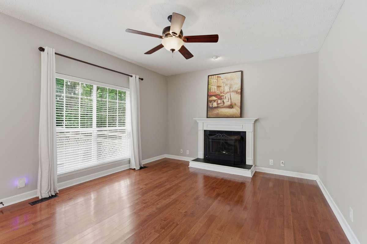 Light-filled living room with hardwood floors, ceiling fan, and a classic fireplace, offering flexible space for a media room, or additional gathering area while maintaining an open flow to the main living spaces.