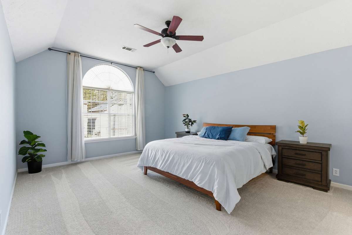 Light-filled owner’s bedroom with vaulted ceilings, soft neutral tones, and an arched window. Directly connected to the owner’s bathroom and walk-in closet for comfort, privacy, and everyday ease.
