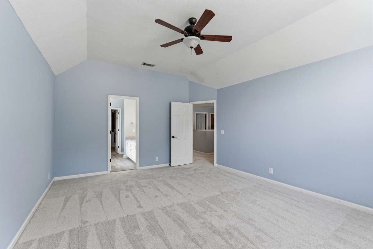 Light-filled owner’s bedroom with vaulted ceilings, soft neutral tones, and an arched window. Directly connected to the owner’s bathroom and walk-in closet for comfort, privacy, and everyday ease.